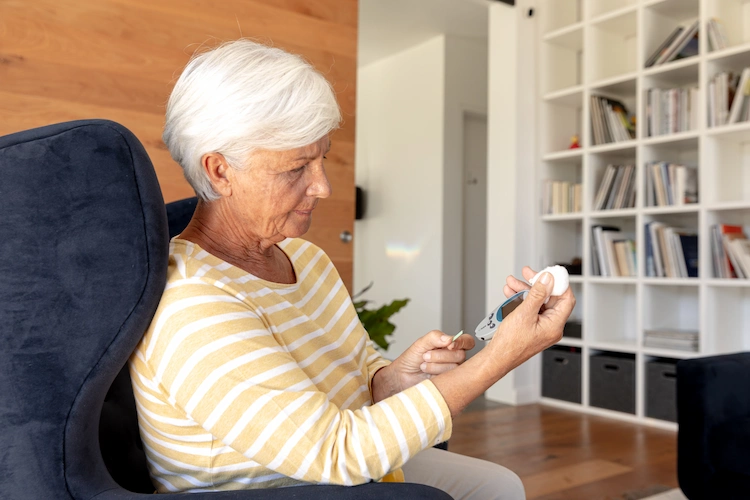 senior woman uses a blood glucose meter at home to measure the blood glucose level in the blood