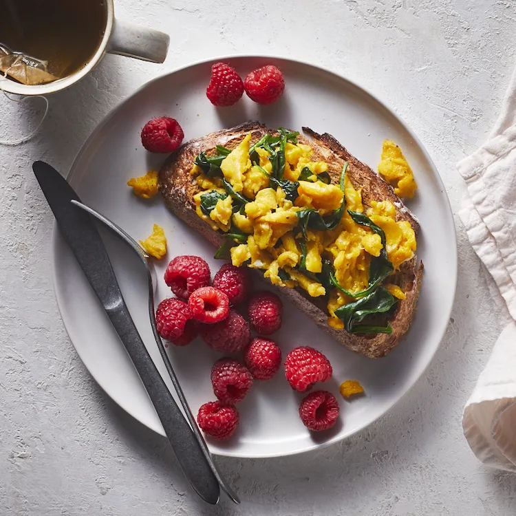 healthy meal consisting of buttered bread with scrambled eggs and spinach in combination with raspberries and green tea